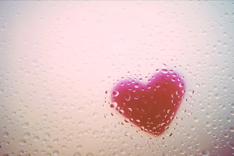 Et hjerte bak et vindu med regn på.