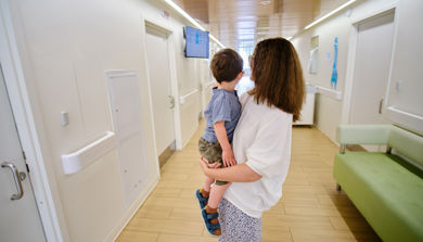 Mor som bærer et barn på armen i en sykehuskorridor