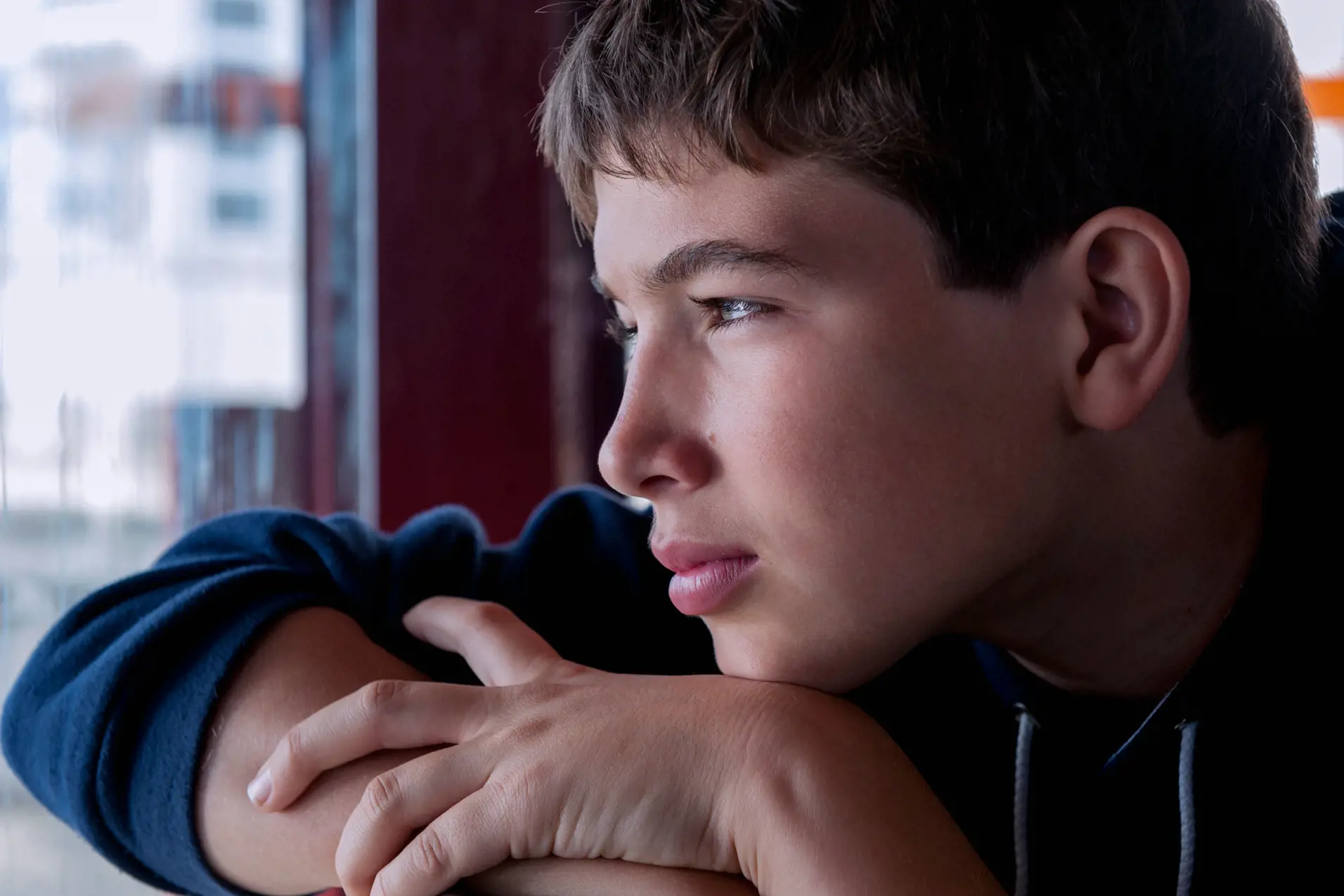 En gutt hviler haken på hånden og ser ut av et vindu