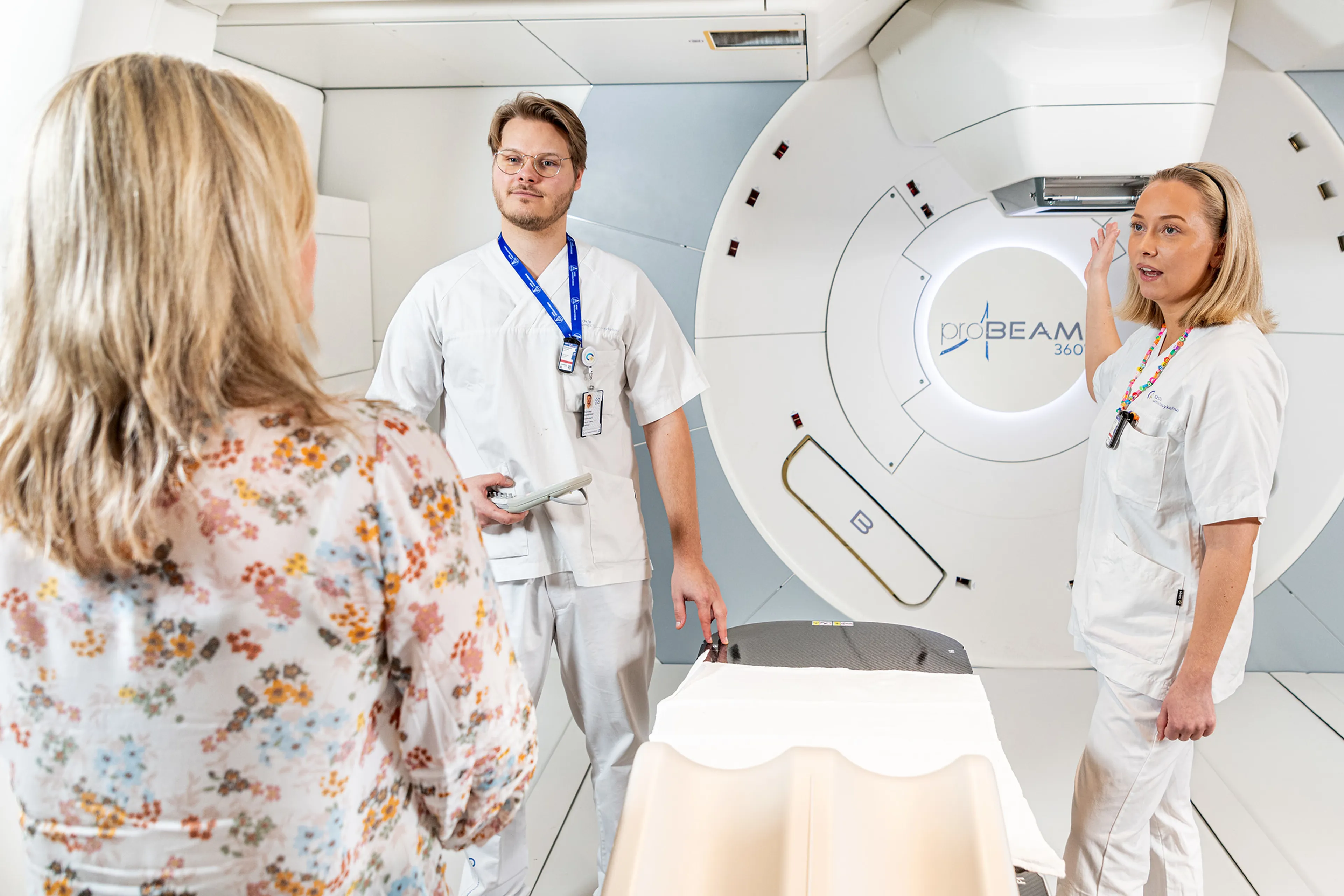 Ansatte står foran en protonterapimaskin og snakker med en pasient
