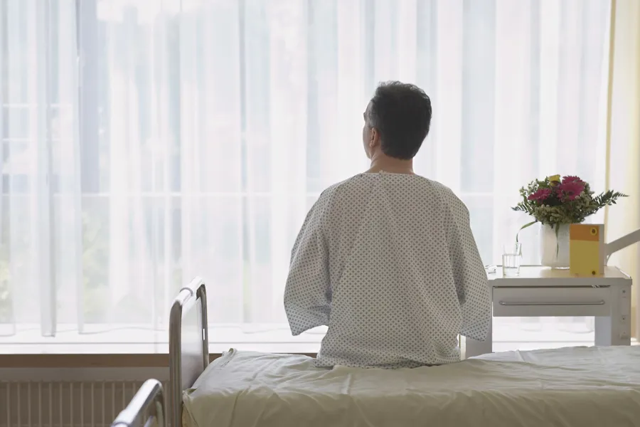 En pasient som sitter på en seng med ryggen mot oss og ser ut av vinduet