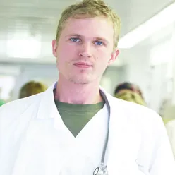 En person kledd i hvitt med stetopskop rundt halsen står foran flere helsearbeidere og ser inn i kameraet.