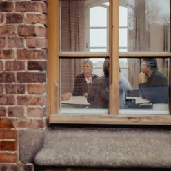 Bildet er tatt inn et vindu hvor man ser tre personer som jobber sammen og konverserer.