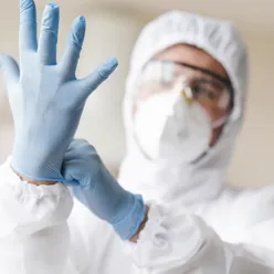 En person i hvit labfrakk og hansker som holder en blå gjenstand