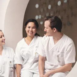 Bilde av to kvinner og en mann i hvit sykehusuniform som ser på hverandre og smiler
