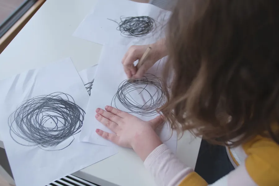 Bakhodet til jente med brunt hår tegner sorte kruseduller på hvitt ark