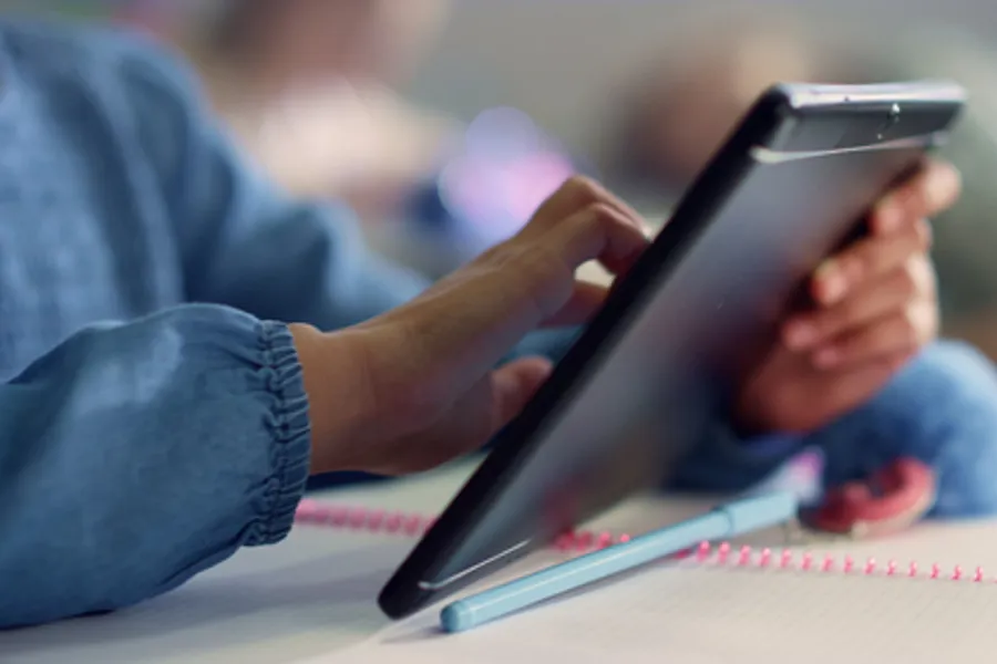 Hånden til en ung person tar på en tablet. Den unge personen har på seg en blå genser. Tableten er i fokus. 