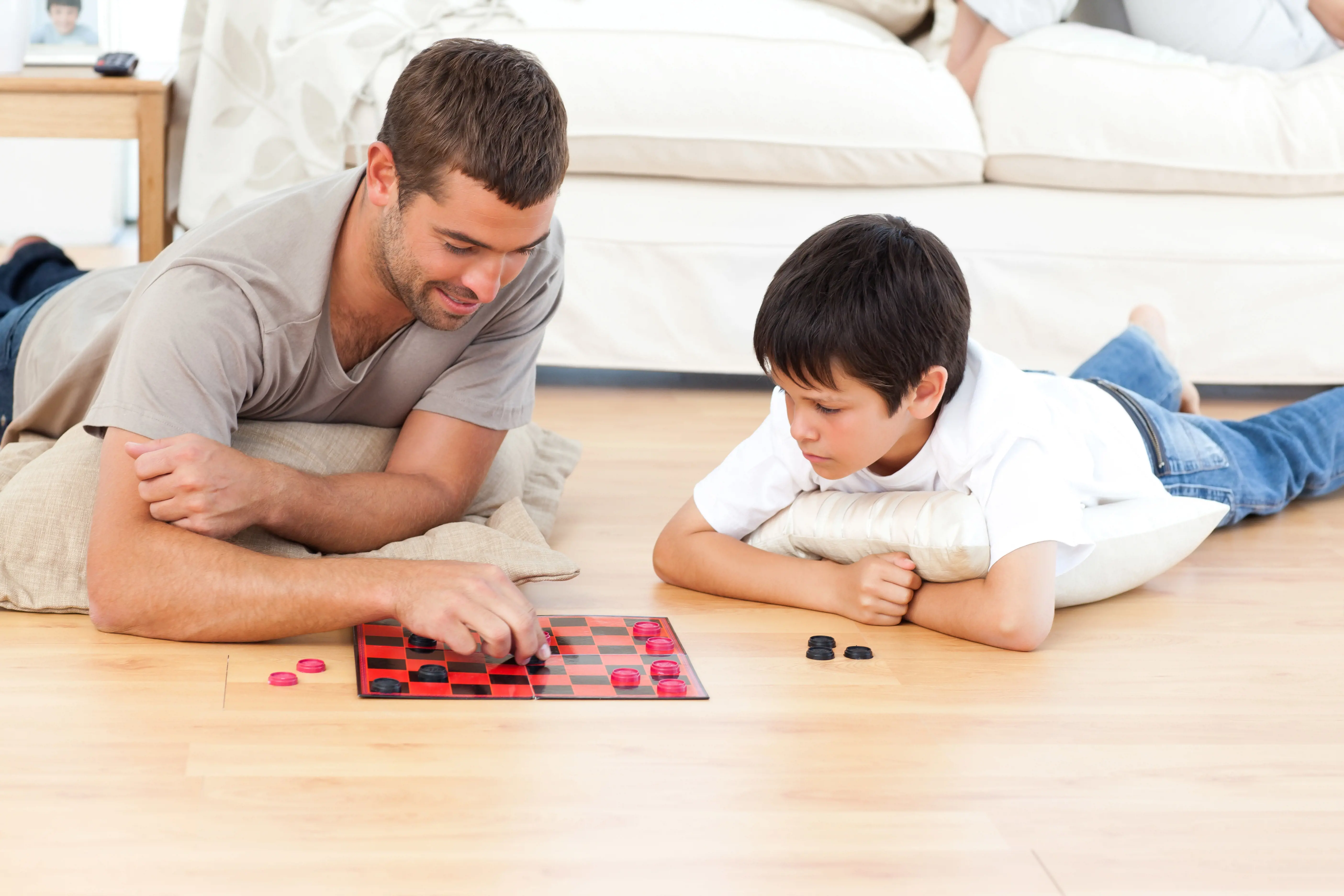 Mann og gutt ligger på gulvet og spiller skakk