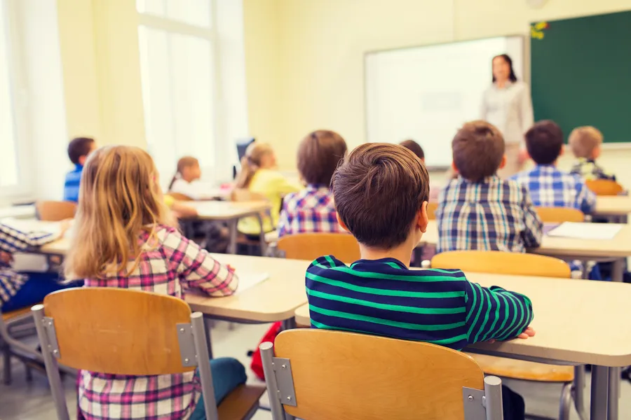 En skoleklasse i barneskolen sett bakfra med lærer foran tavla