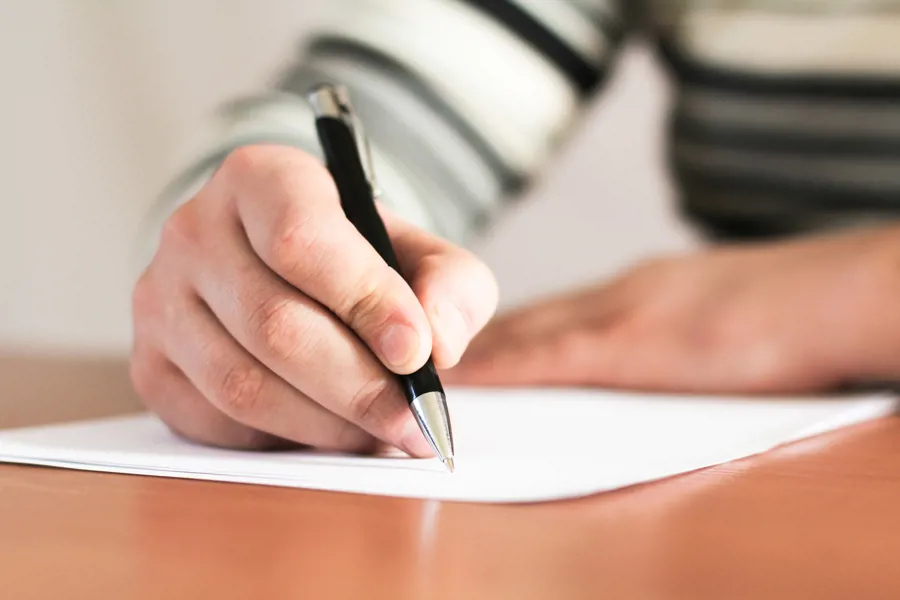 En hånd som holder en pen skrivende på papir.