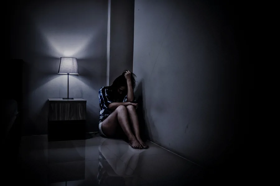 En person sitter på gulvet inntil en vegg og ser ned i knærne sine.