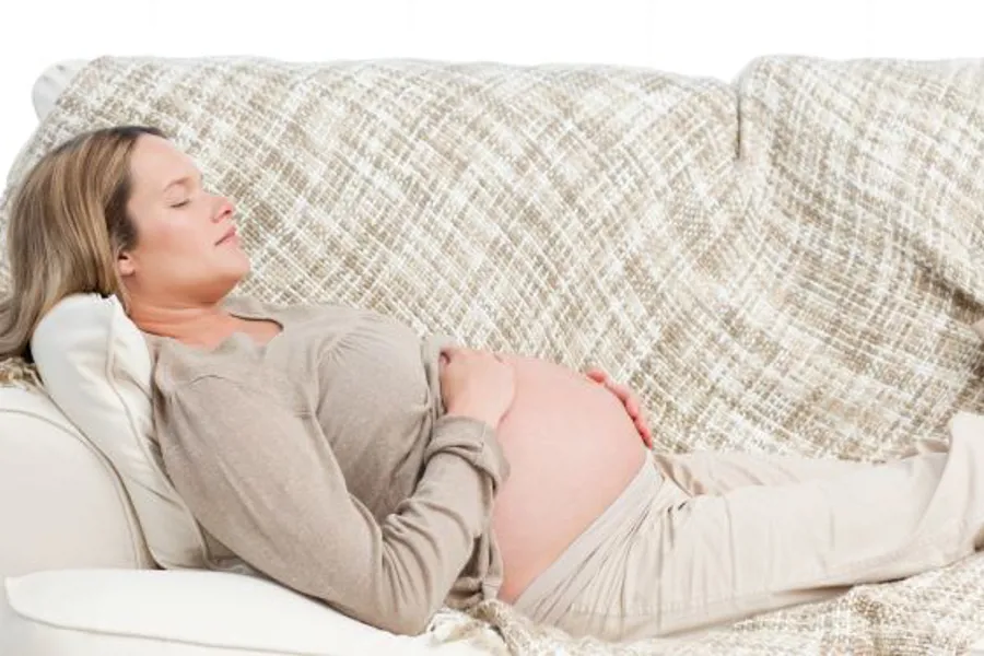 En gravid kvinner ligger på en sofa og holder på magen sin.