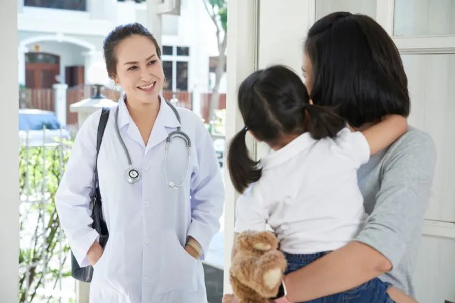 En lege som smiler til en mor som holder sin datter.