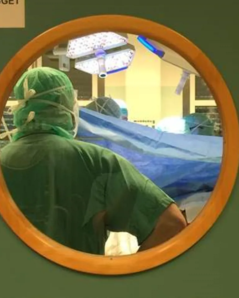 En kirurg som oprerer sett gjennom et vindu i døren til operasjonssalen.