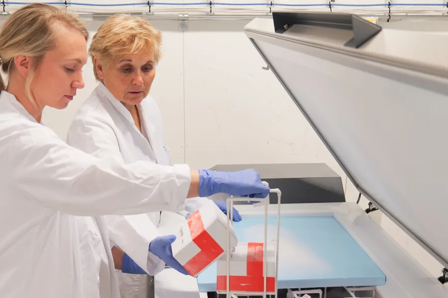 To i hvite frakker som jobber med biobankprøver i en stor maskin.