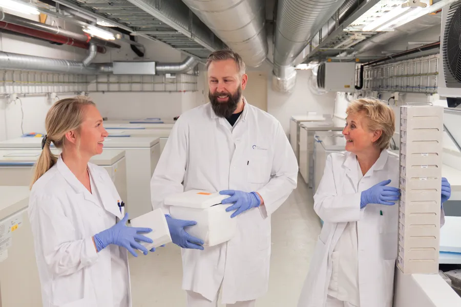 Tre i hvite frakker stående i et laboratorium.