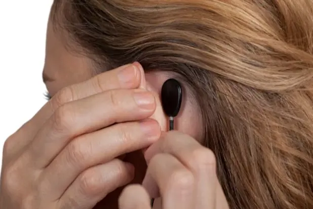 Detaljbilde av en kvinne som fester en liten, svart mottaker på huden bak øret-