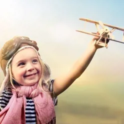 En jente ikledd en gammeldags flygerlue holder opp et lekefly. Hun smiler.