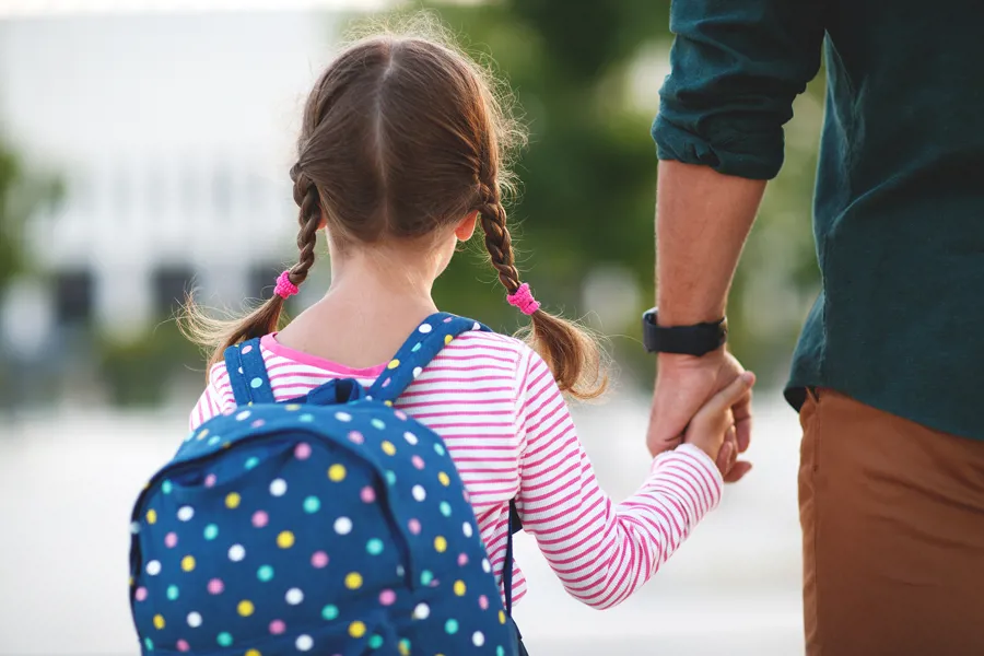 EI jente med fletter og skolesekk leier pappa på vei til skolen.