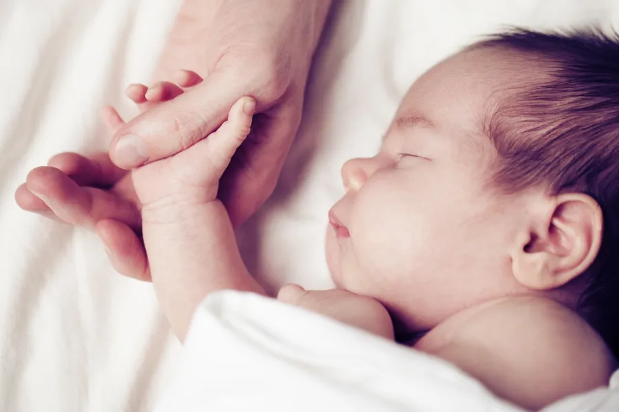 Baby som holder mors hånd.