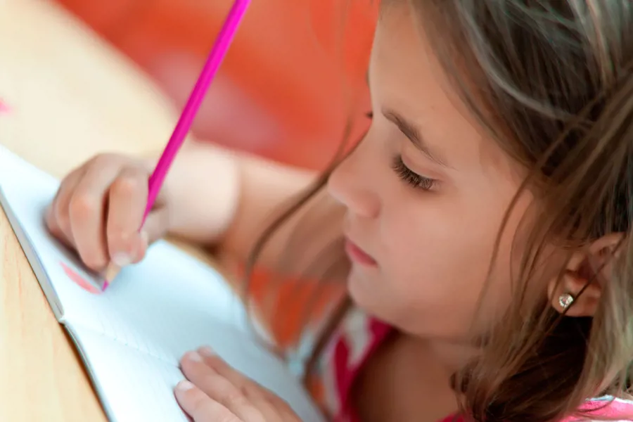 Skoleelev som skriver med en rosa blyant i en skrivebok.