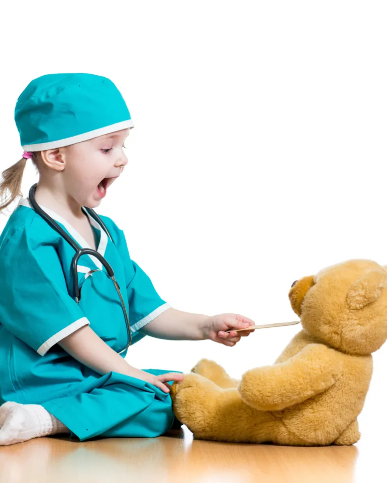 En ung jente i grønne sykehusklær som leker doktor med en bamse
