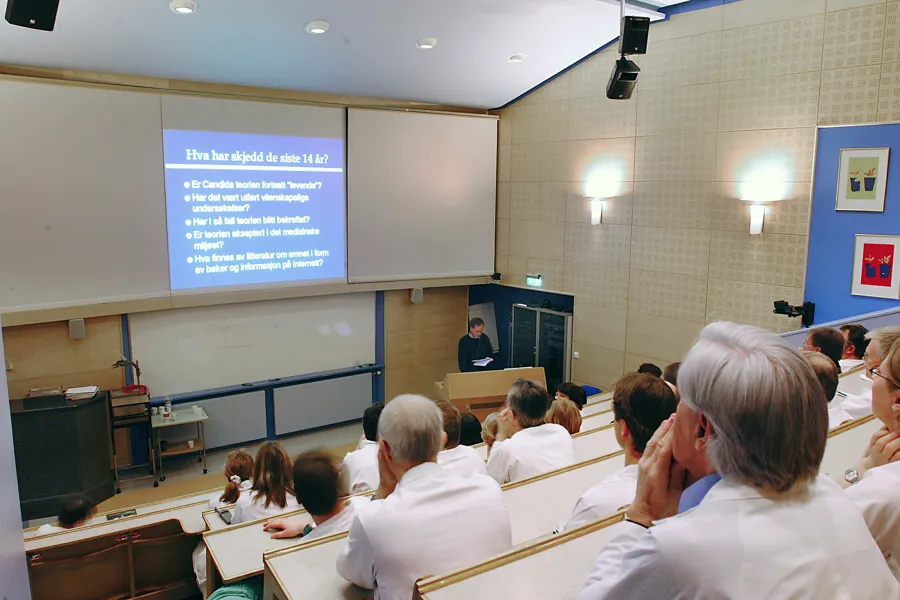 En gruppe mennesker i hvite frakker følger en forelesning i et auditorium